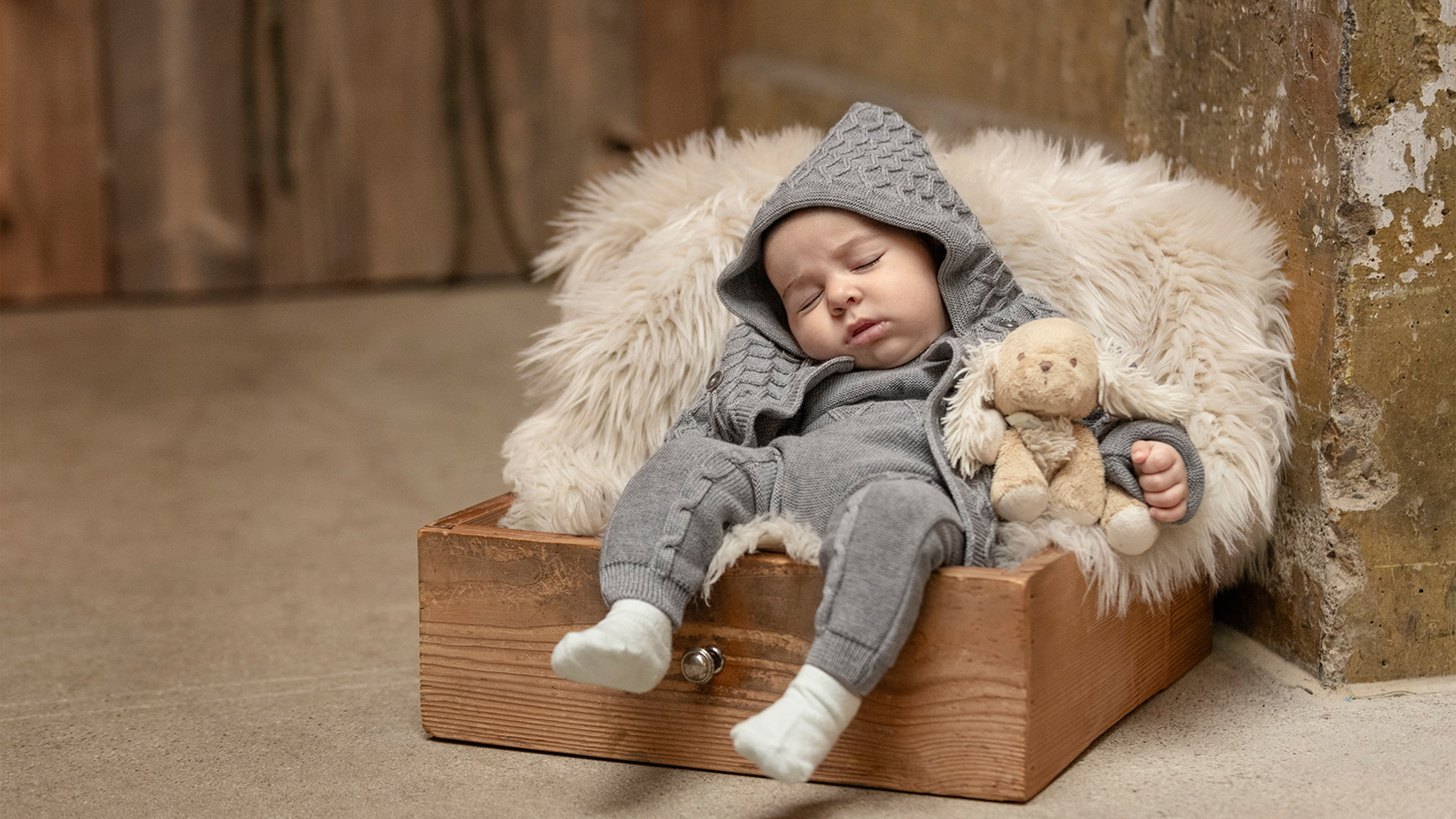 Schlafendes Baby mit grauer Strickkleidung in einer Kiste liegend mit Kuscheltier