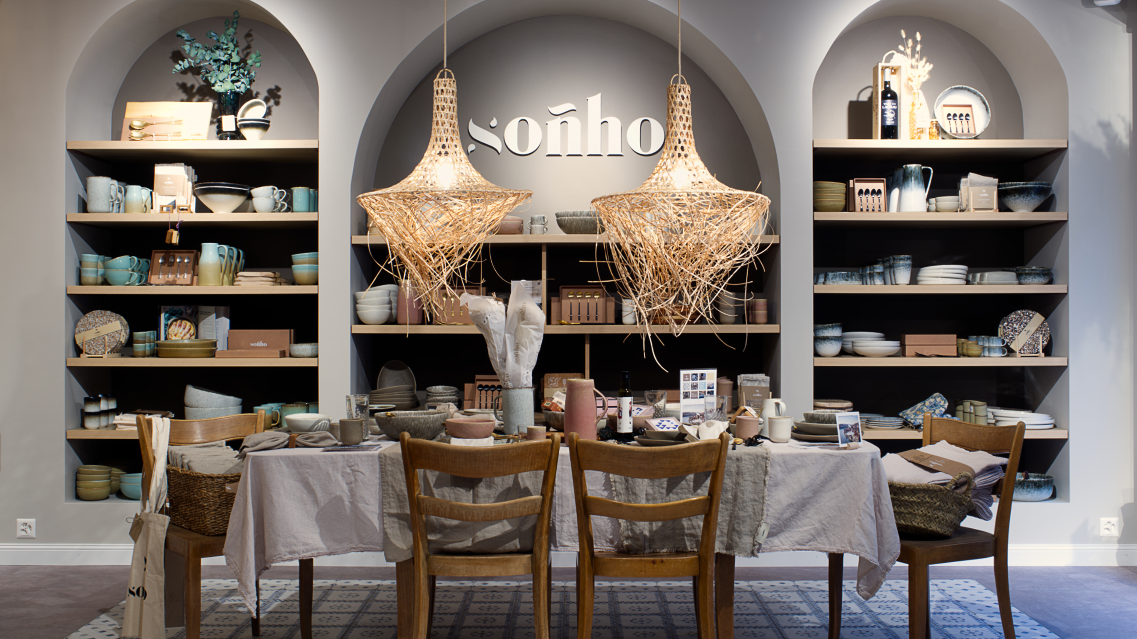 großer Esstisch mit Stühlen, dahinter ein Regal, von oben herab zwei große Lampen