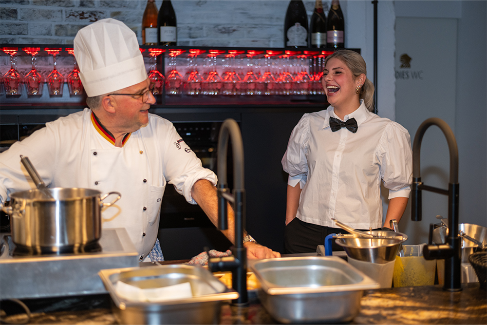 Ein Koch und eine Frau stehen in der Küche und lachen sich an 