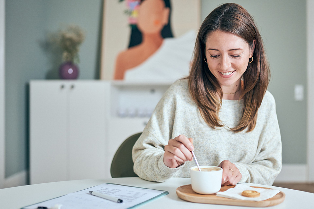 Lachende Frau rührt am Tisch einen Kaffee