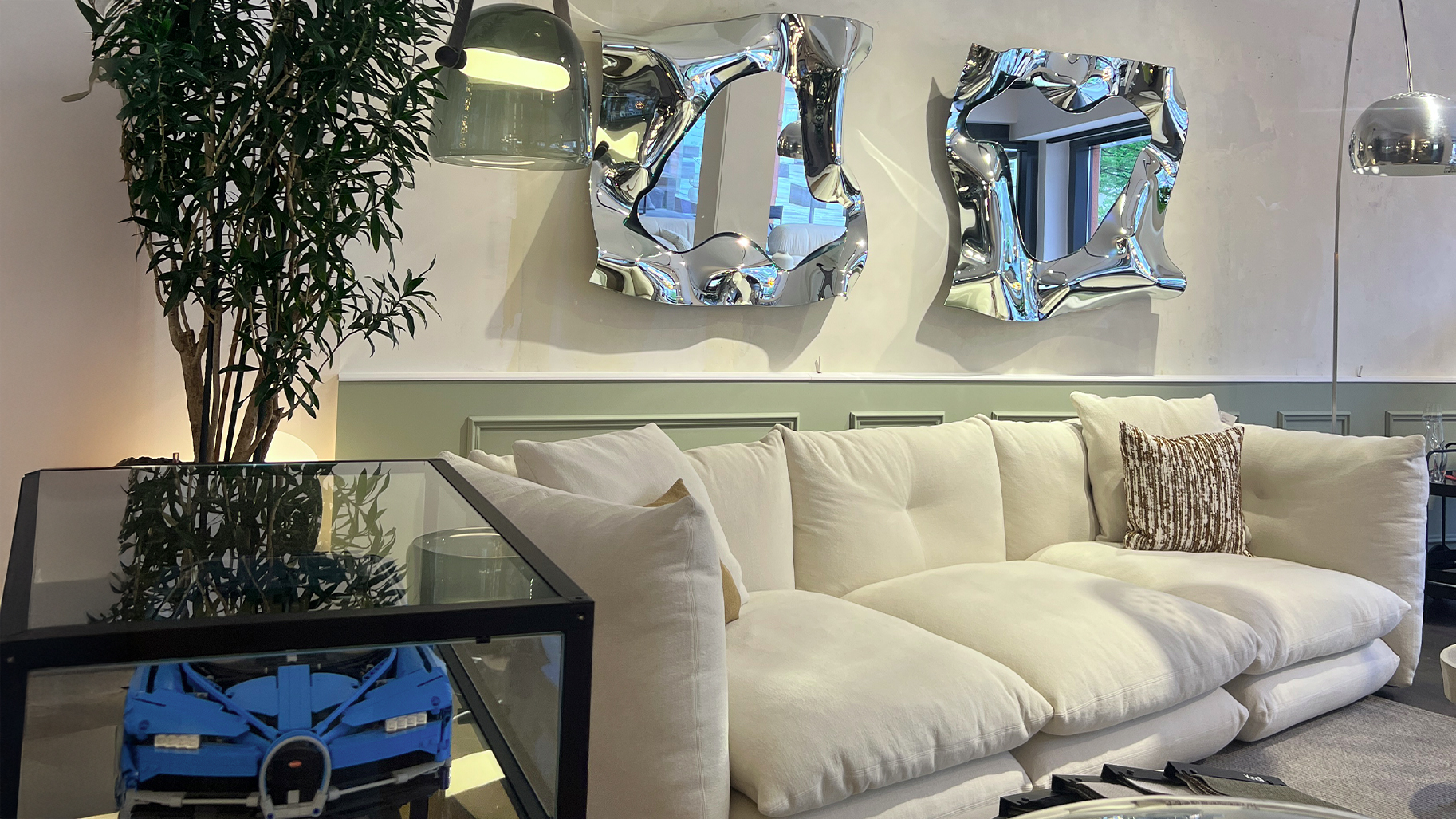 Modernes Wohnzimmer-Arrangement im Albert Grimm Studio G&ouml;ppingen &ndash; Exklusives Design-Sofa kombiniert mit k&uuml;nstlerischen Wandspiegeln und hochwertiger Lichtgestaltung am Schillerplatz.