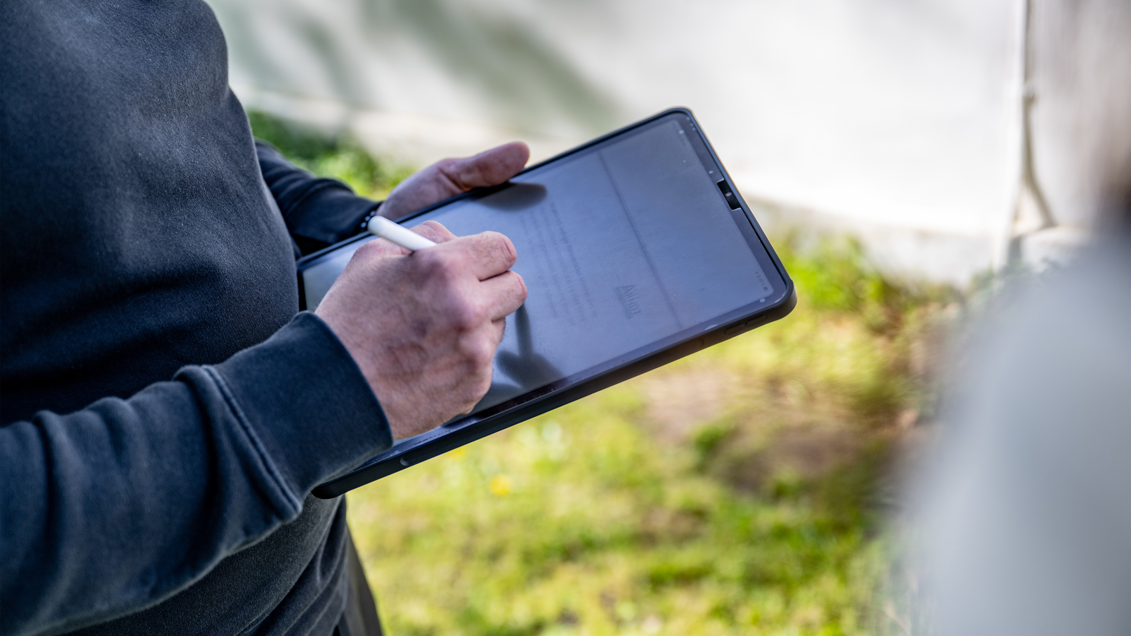 Eine Person hat ein IPad in der Hand und notiert etwas.