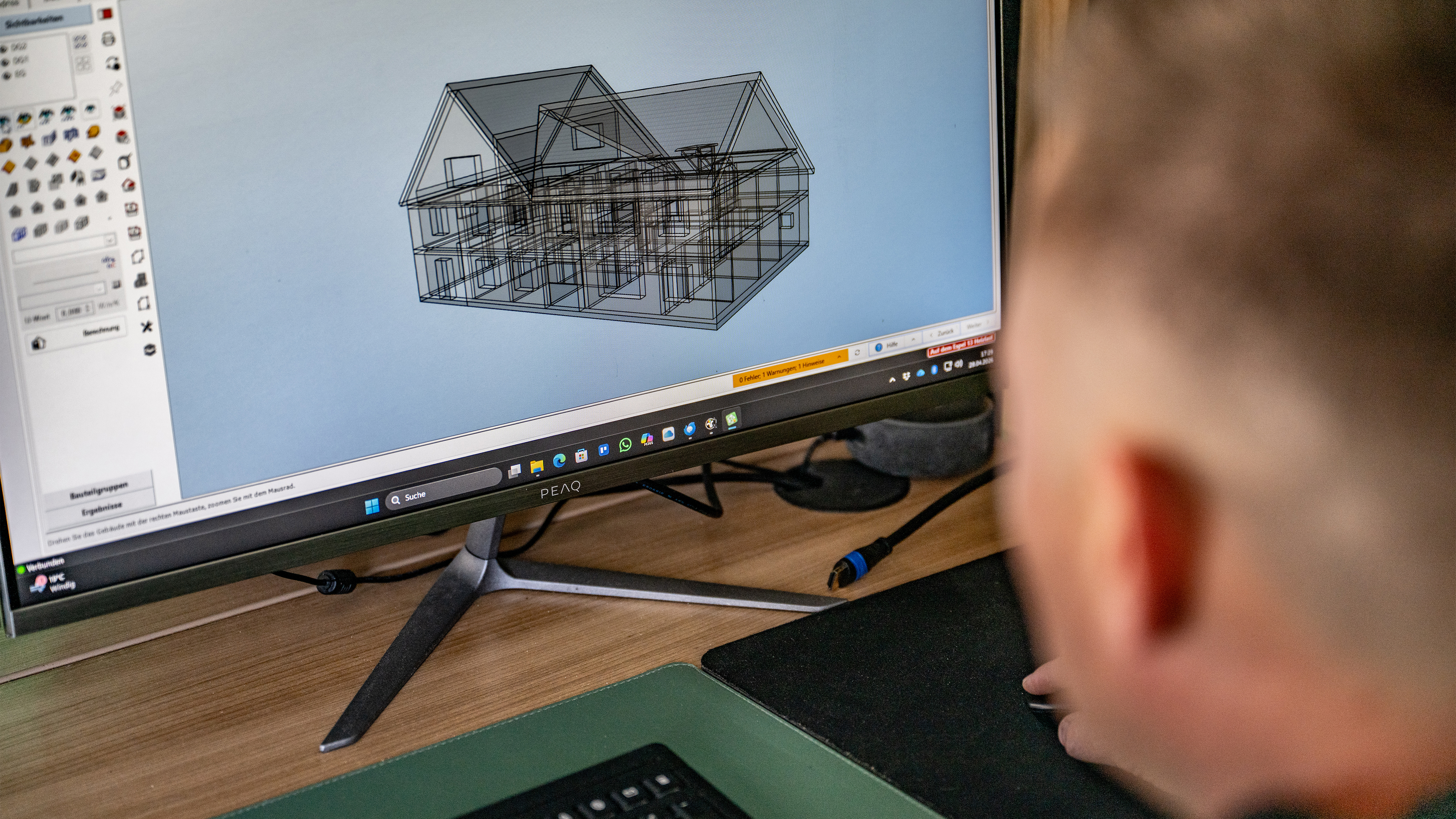 Person betrachtet und bearbeitet 3D-Hausmodell am Computer.