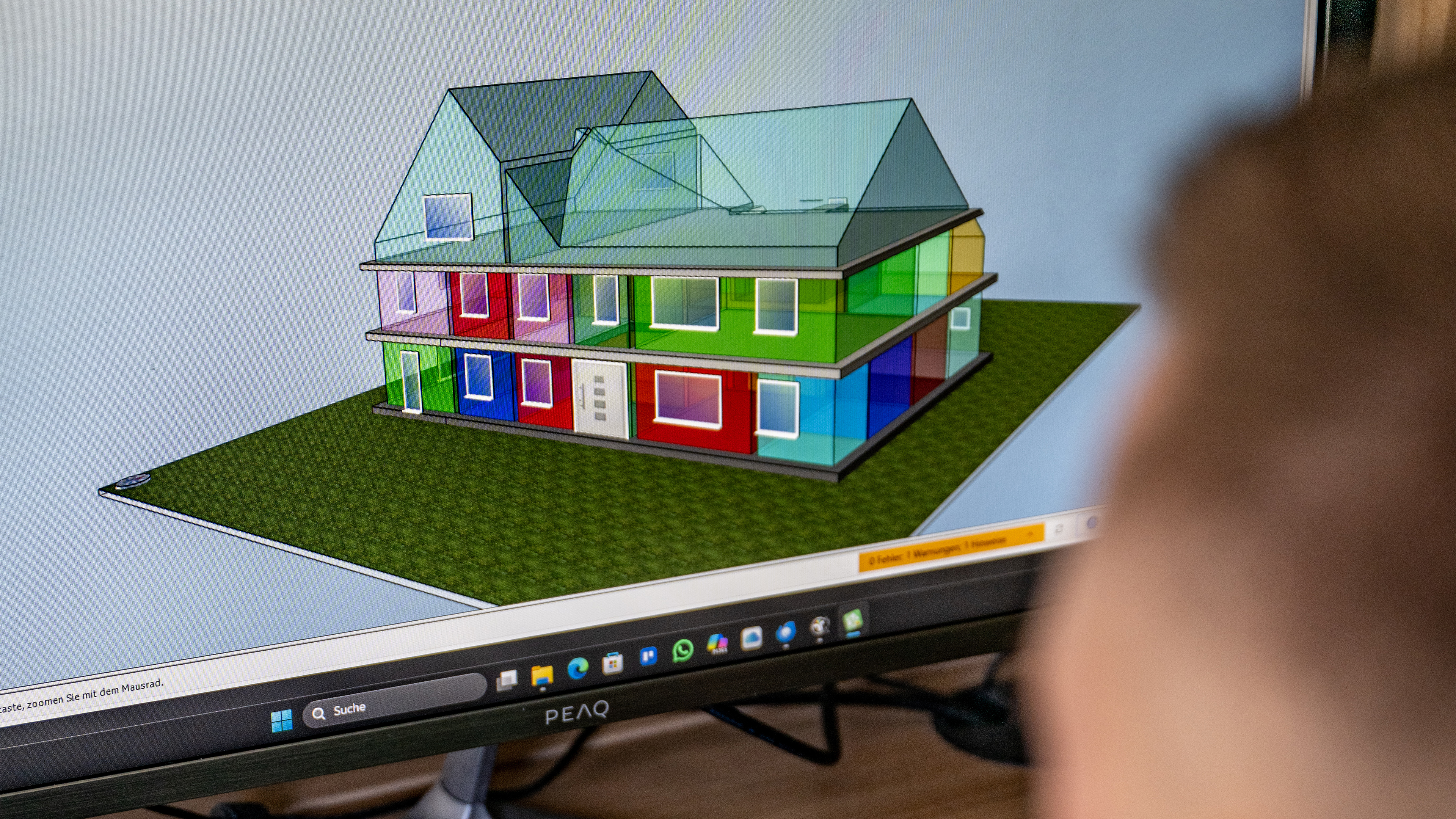 Person betrachtet farbiges 3D-Hausmodell am Computer.