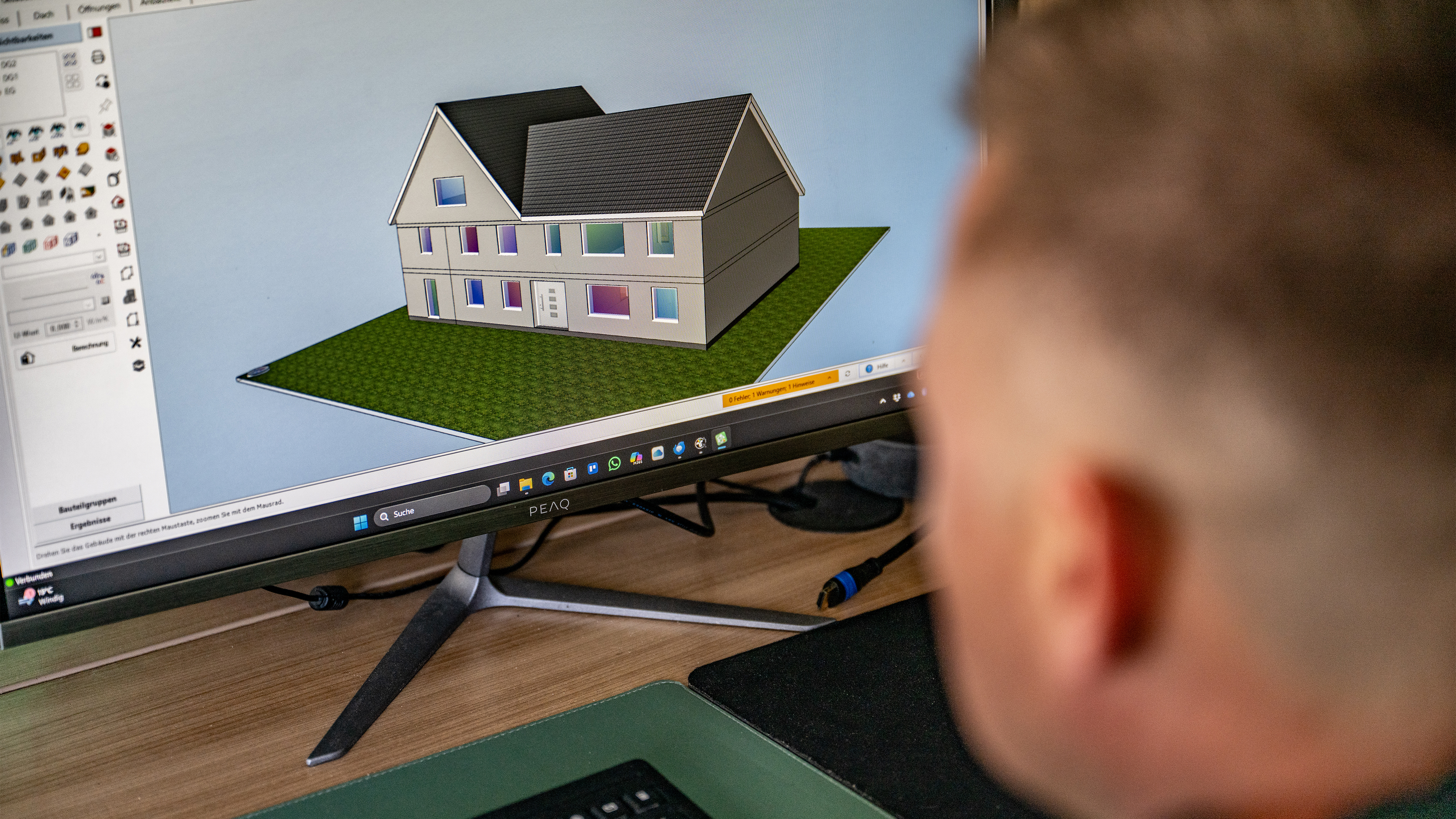 Person betrachtet farbiges 3D-Hausmodell am Computer.