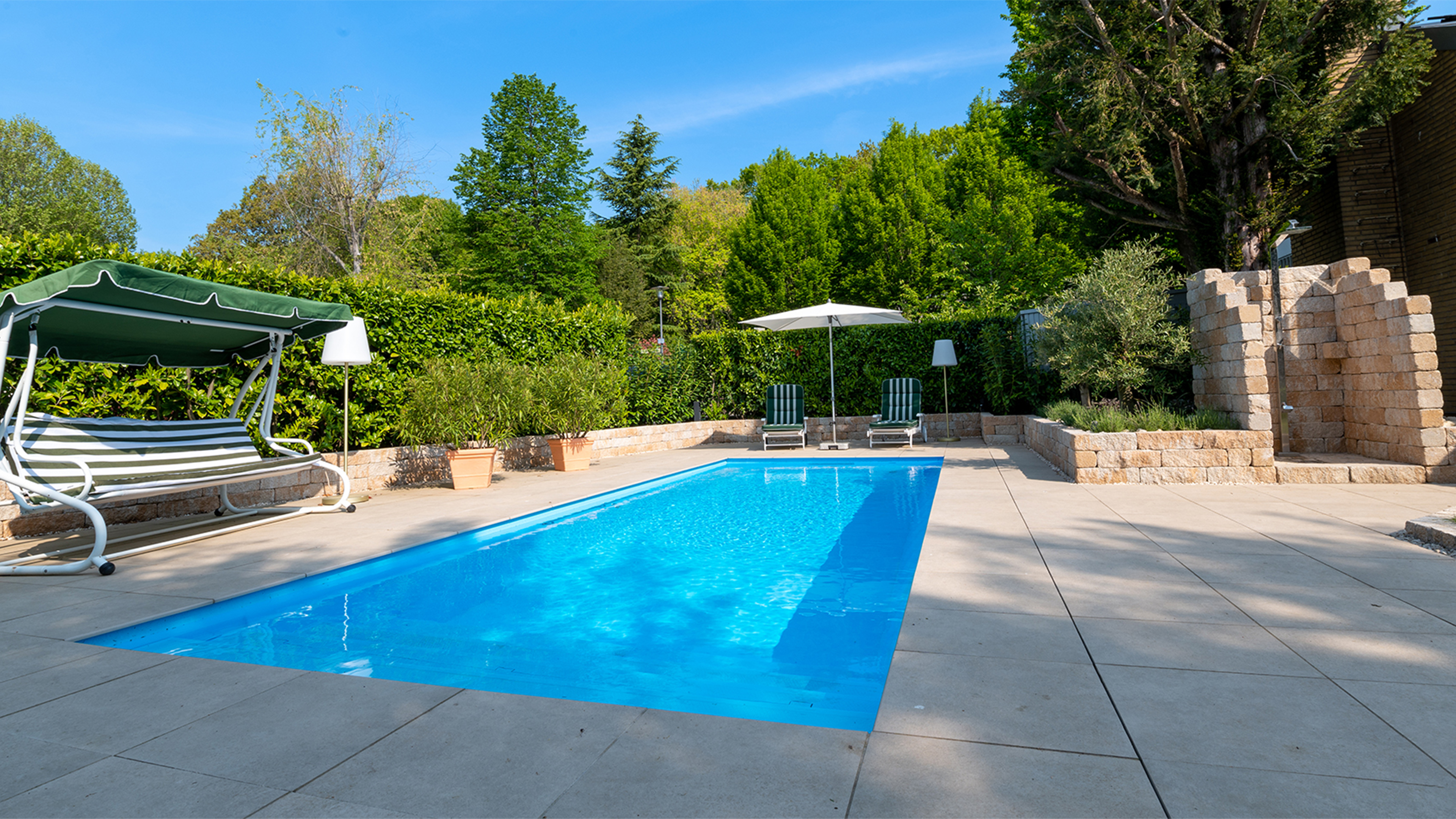 Pool mit gemauerter Dusche aus Naturstein und einer Hollywood Schaukel