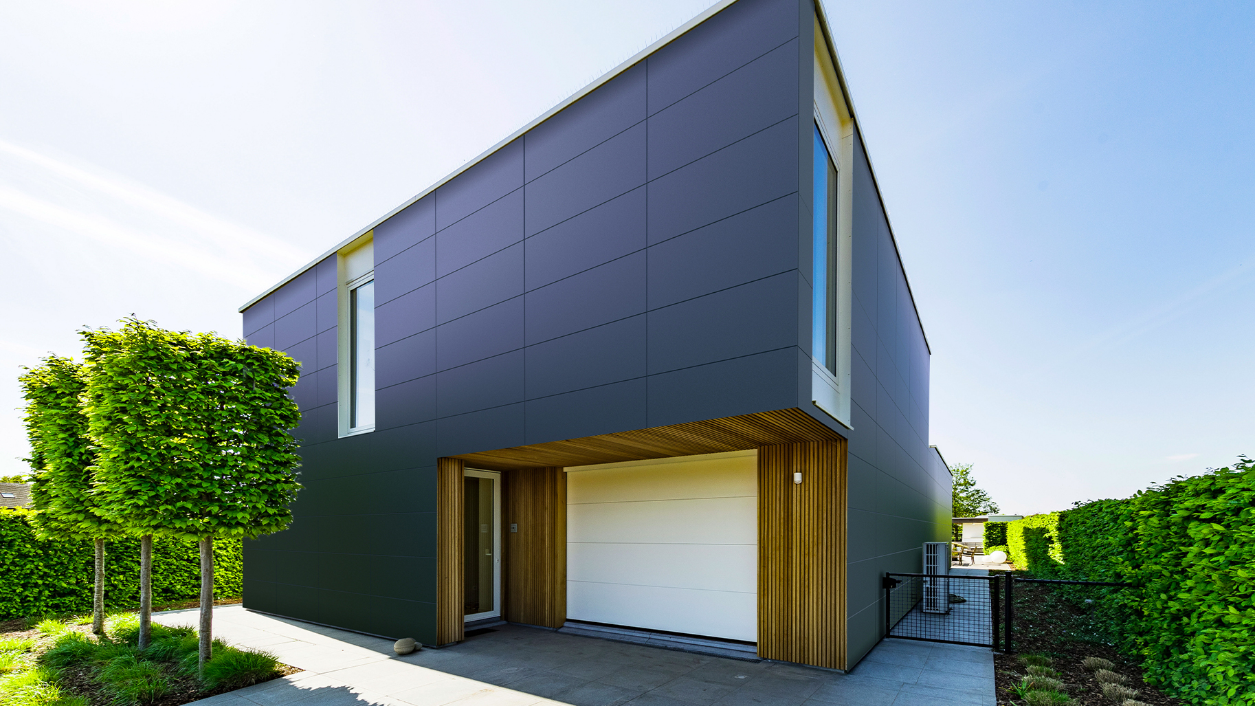 Modernes Wohnhaus mit anthrazitfarbenen Fassadenplatten und vertikalen Holzlamellen am Eingangsbereich.