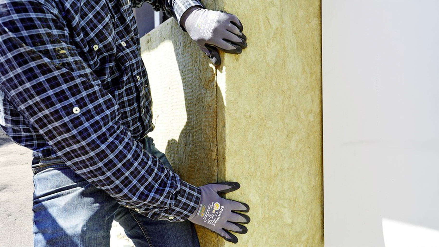 Ein Handwerker setzt eine feste Mineralwolle-Dämmplatte an einer Außenwand ein.
