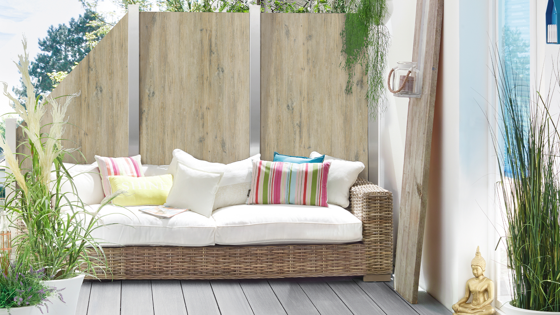 Sichtschutzpaneele in heller Eichenoptik begrenzen eine wohnlich gestaltete Terrasse mit weißem Loungesofa.