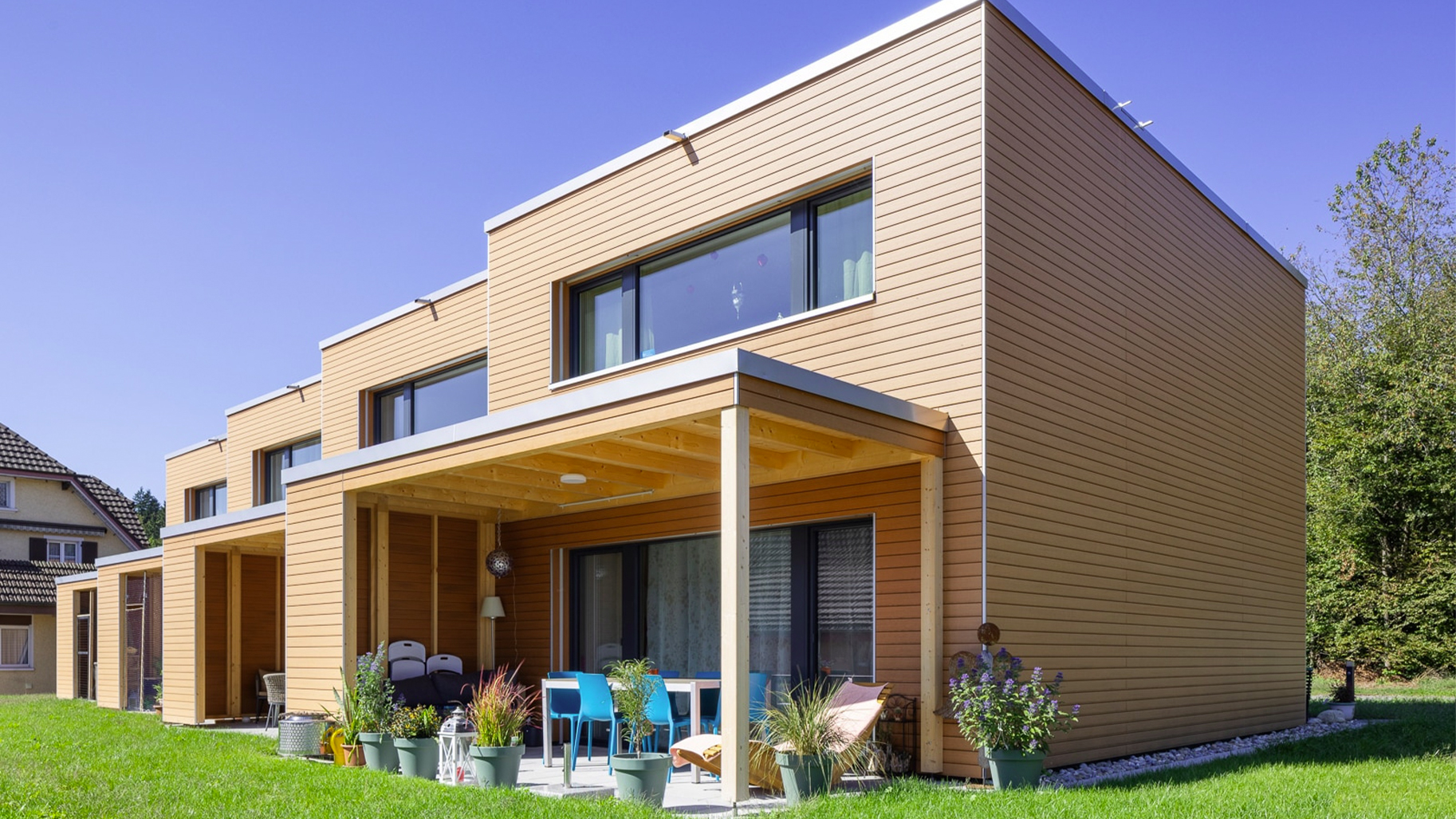 Moderne Reihenhäuser mit horizontaler Fassadenbekleidung in warmer Holzoptik und überdachten Terrassen.