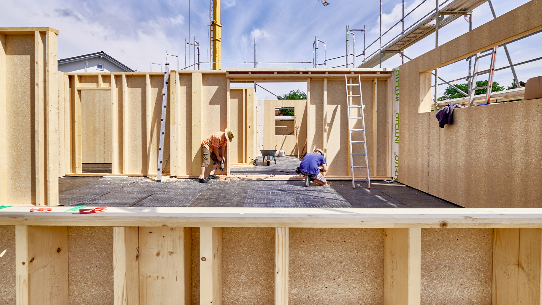 Zwei Handwerker montieren Holzrahmenwände mit Holzwerkstoffplatten auf einer Baustelle.