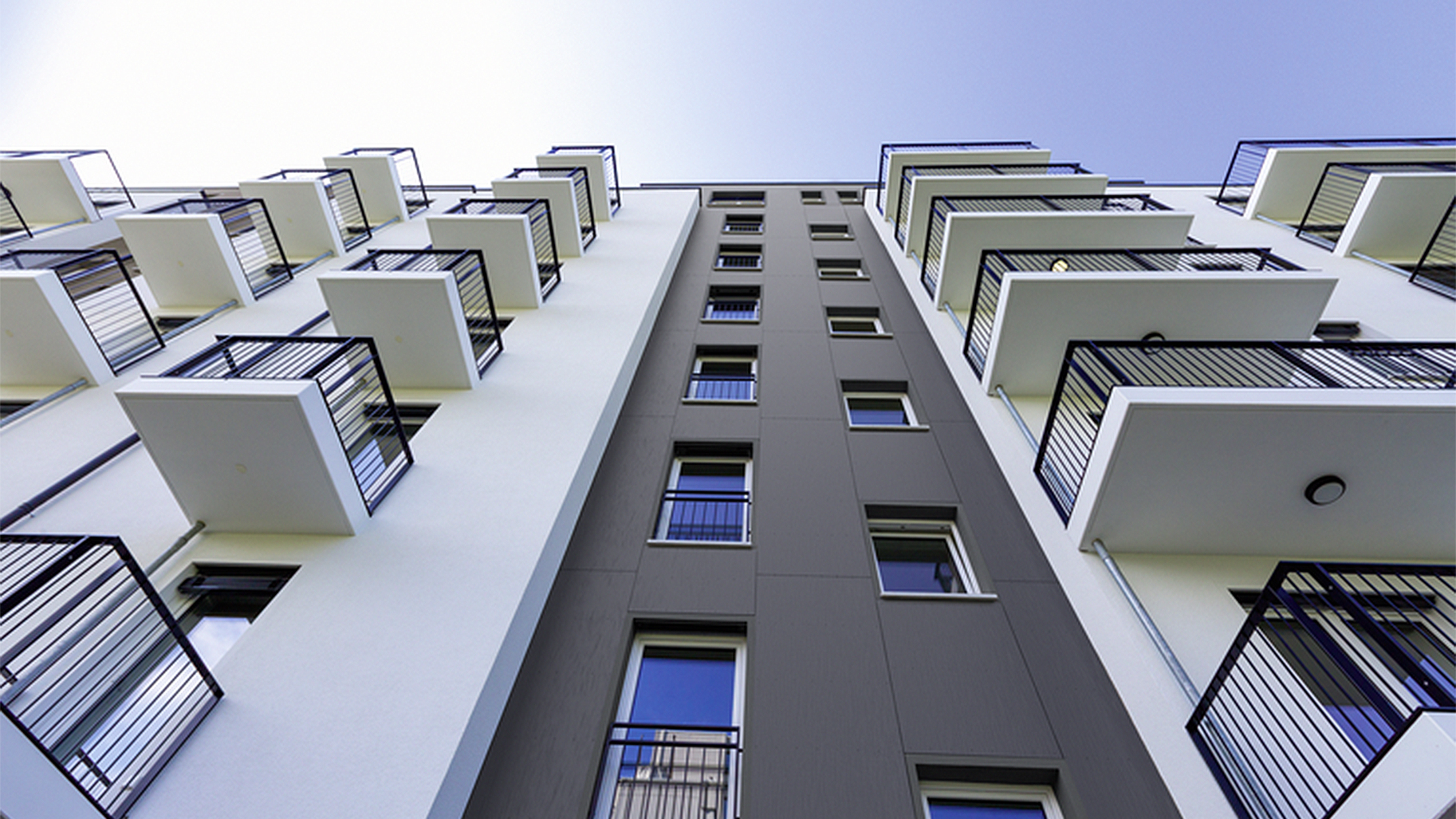 Mehrgeschossiges Wohngebäude mit weißer Putzfassade, anthrazitfarbener Mittelzone und auskragenden Balkonen.
