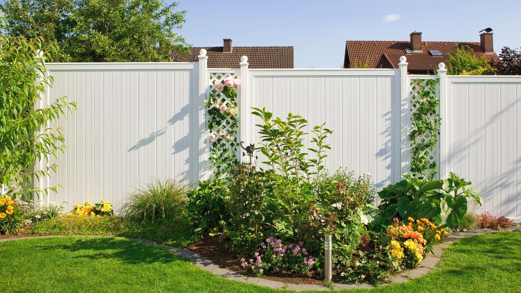 Weißer Sichtschutzzaun mit Rankgittern, Rosen und üppiger Bepflanzung in einem gepflegten Garten.