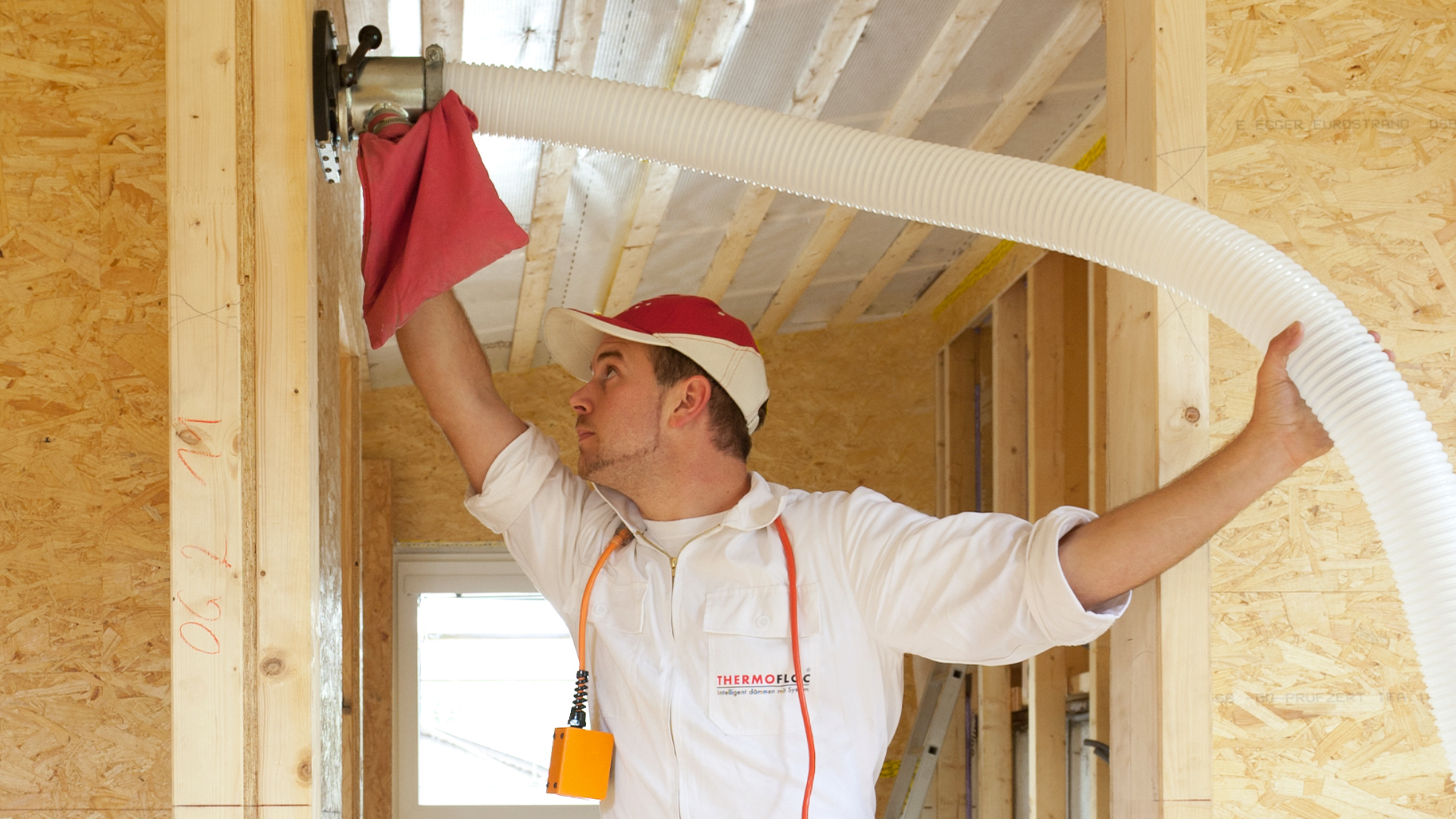 Ein Fachhandwerker bläst Zellulosedämmung über einen Schlauch in eine Holzrahmenwand ein.