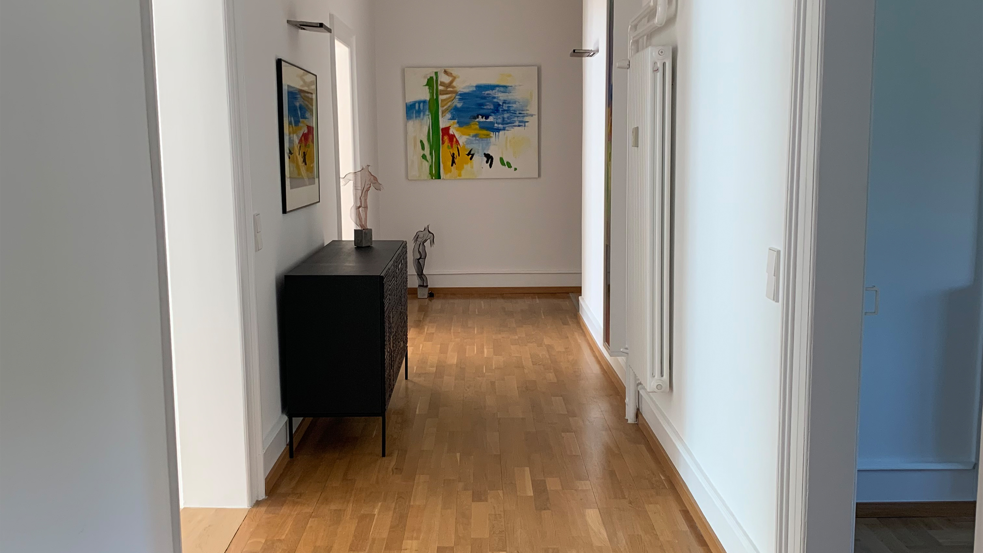 Schmaler, heller Flur mit Holzboden und Wandbild