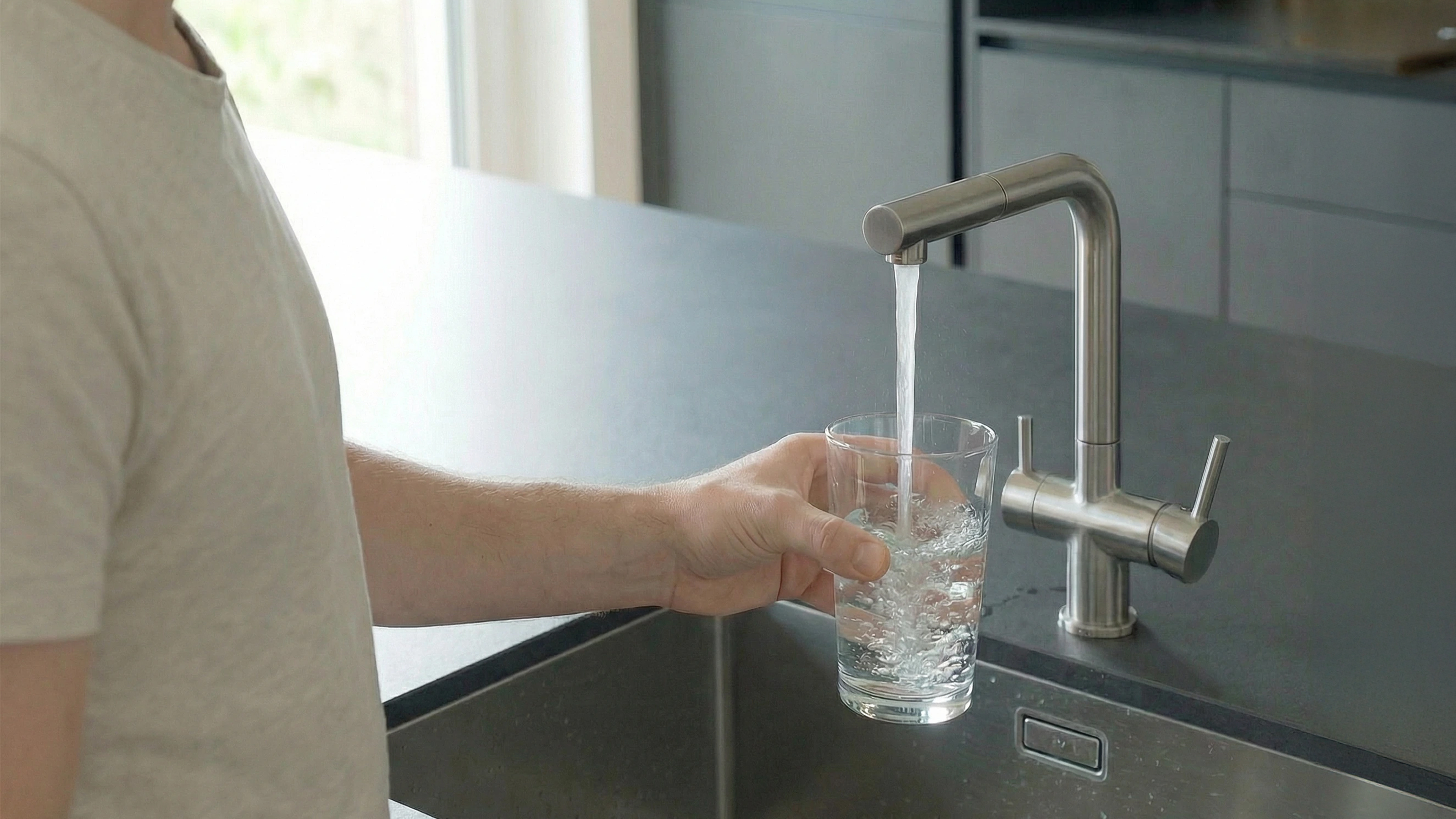 Glas wird an einem Küchenwasserhahn mit Leitungswasser gefüllt