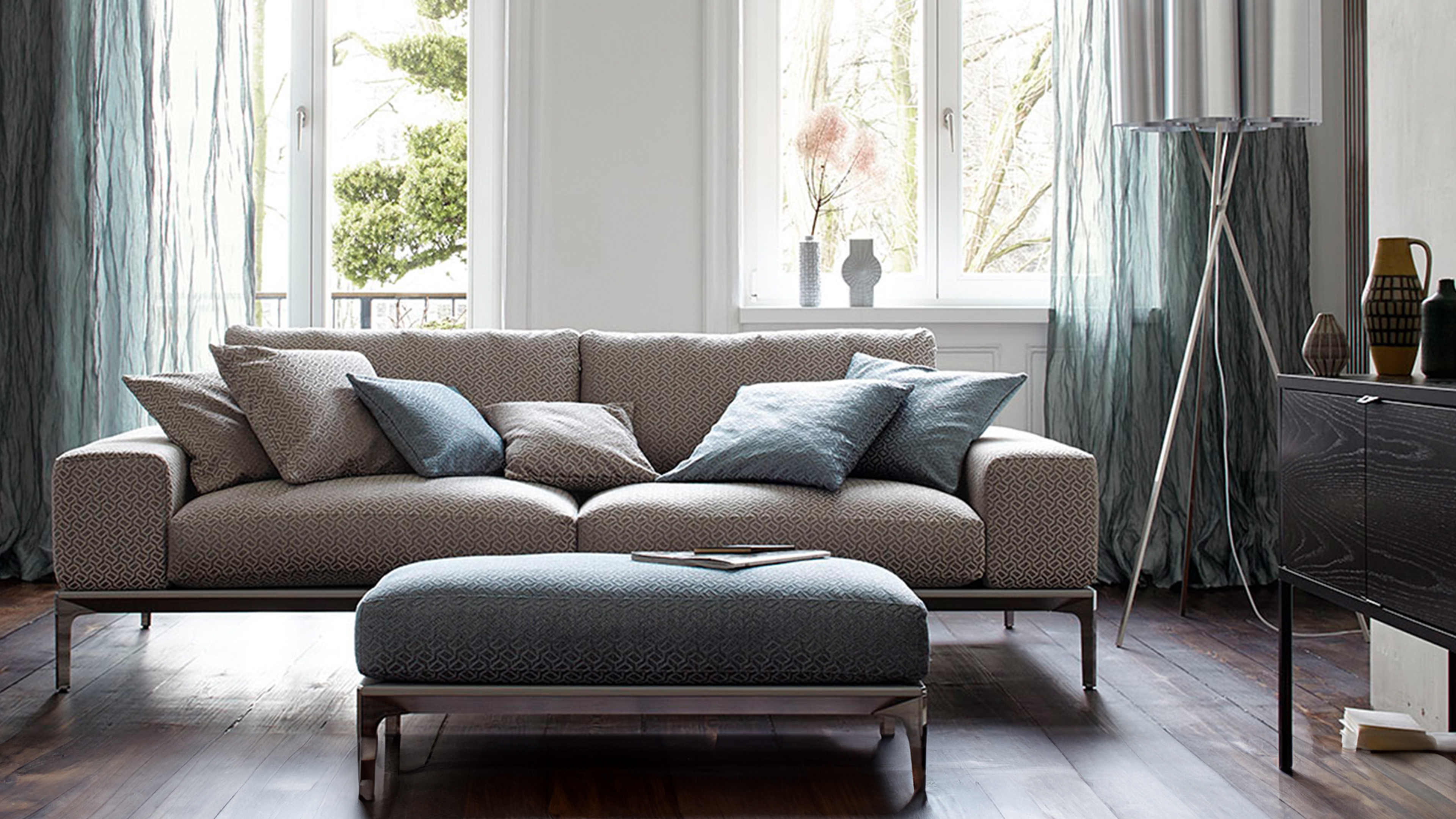 Modern eingerichtetes Wohnzimmer mit grau brauner Couch und grünen Kissen und Vorhängen von Esther Fingerle Interiordesign