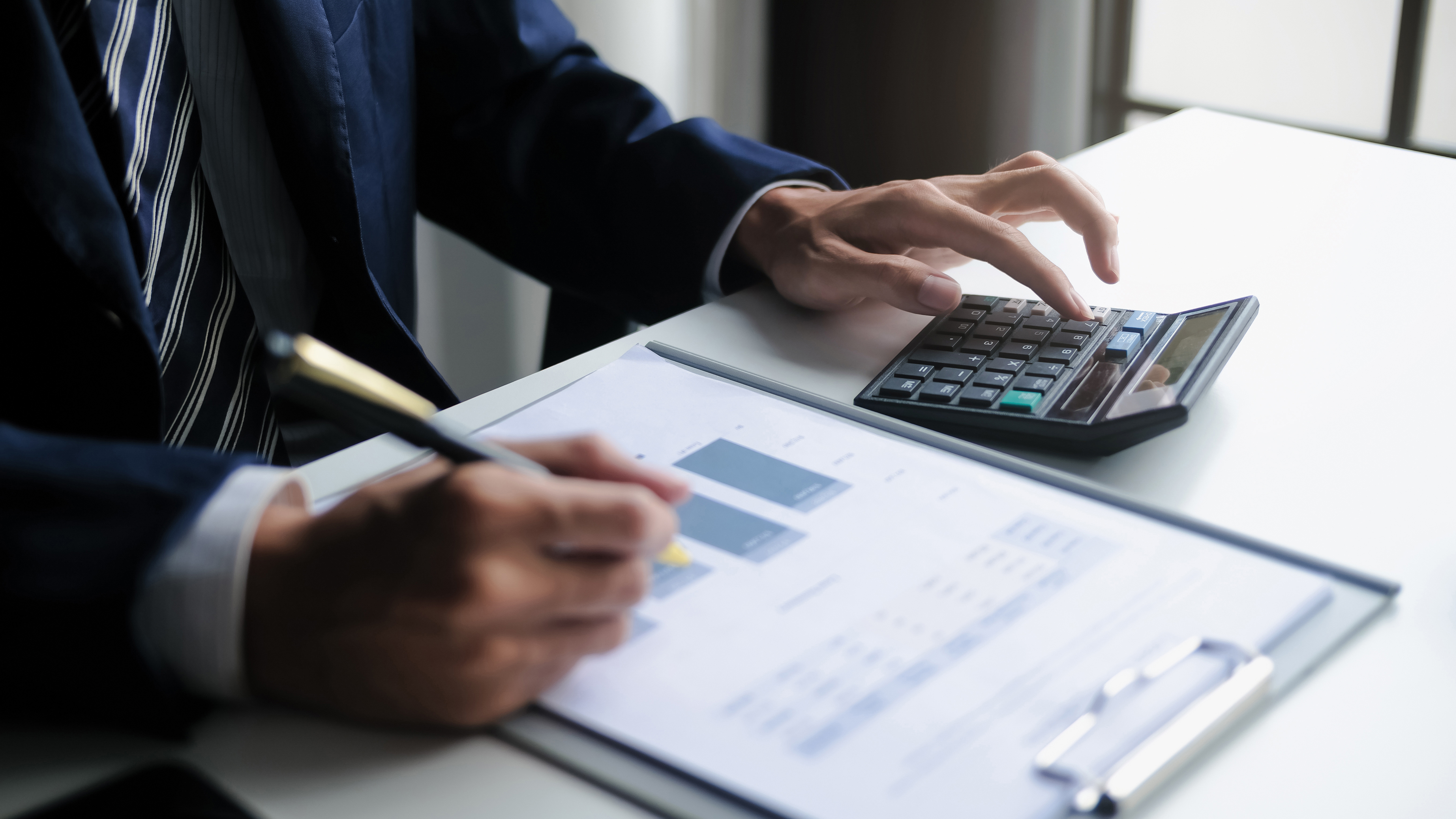 Mann hat einen Stift in der Hand und auf dem Tisch liegen ein Taschenrechner sowie eine Kladde mit Dokumenten