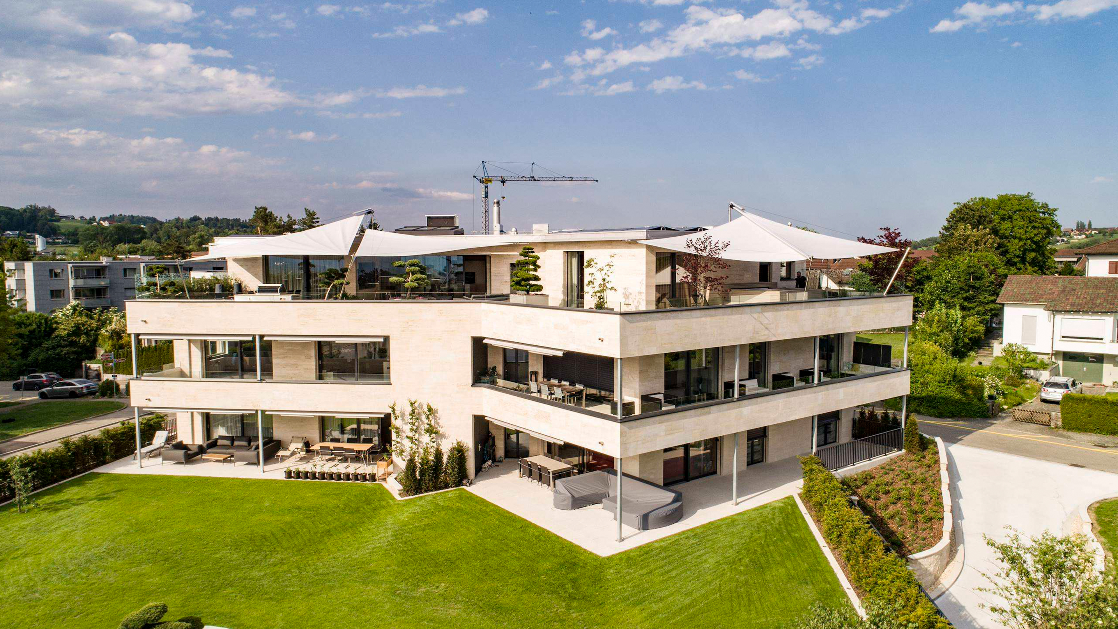 Mehrfamilienhaus mit heller Front und Dachterassen mit grißen Sonnensegeln