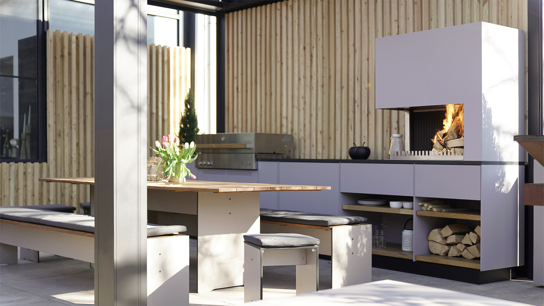 Eine Frau deckt den Tisch im Outdoor-Showroom von Feuerloft Luxembourg neben einer ausgestatteten Gartenküche