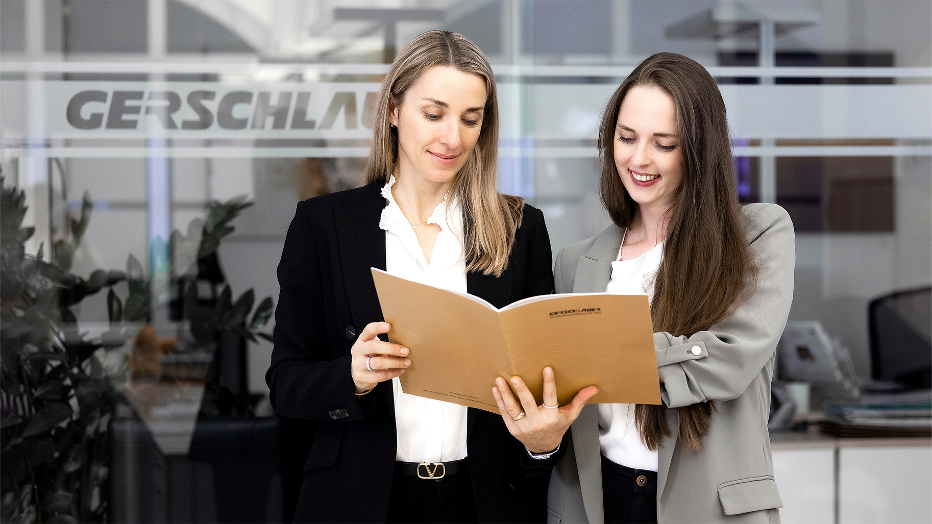 Zwei Immobilienmaklerinnen von Gerschlauer Immobilien in München prüfen Verkaufsunterlagen und ein Exposé im Büro.