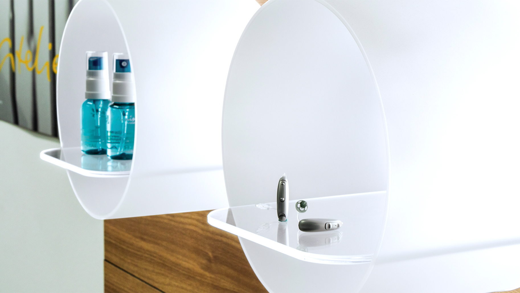 Moderne Pr&auml;sentation von H&ouml;rger&auml;ten und Pflegeprodukten bei M&auml;nning h&ouml;ren-sehen-erleben. Die Nahaufnahme zeigt filigrane H&ouml;rsysteme auf transparenten Ablagen, die die diskrete Versorgung in der P&auml;daudiologie und den Einsatz pr&auml;ziser 3D-Ohrscan-Technologie f&uuml;r individuellen Geh&ouml;rschutz unterstreichen.