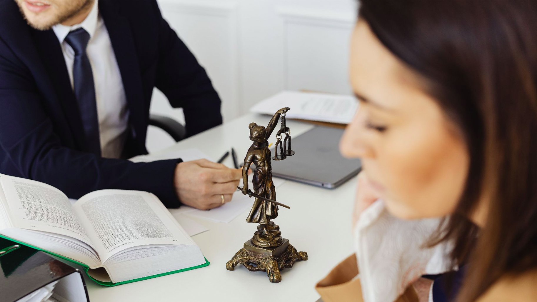 Beratungsgespräch mit Gesetzbuch und Justitia-Figur zu einer rechtlich komplexen Immobiliensituation.