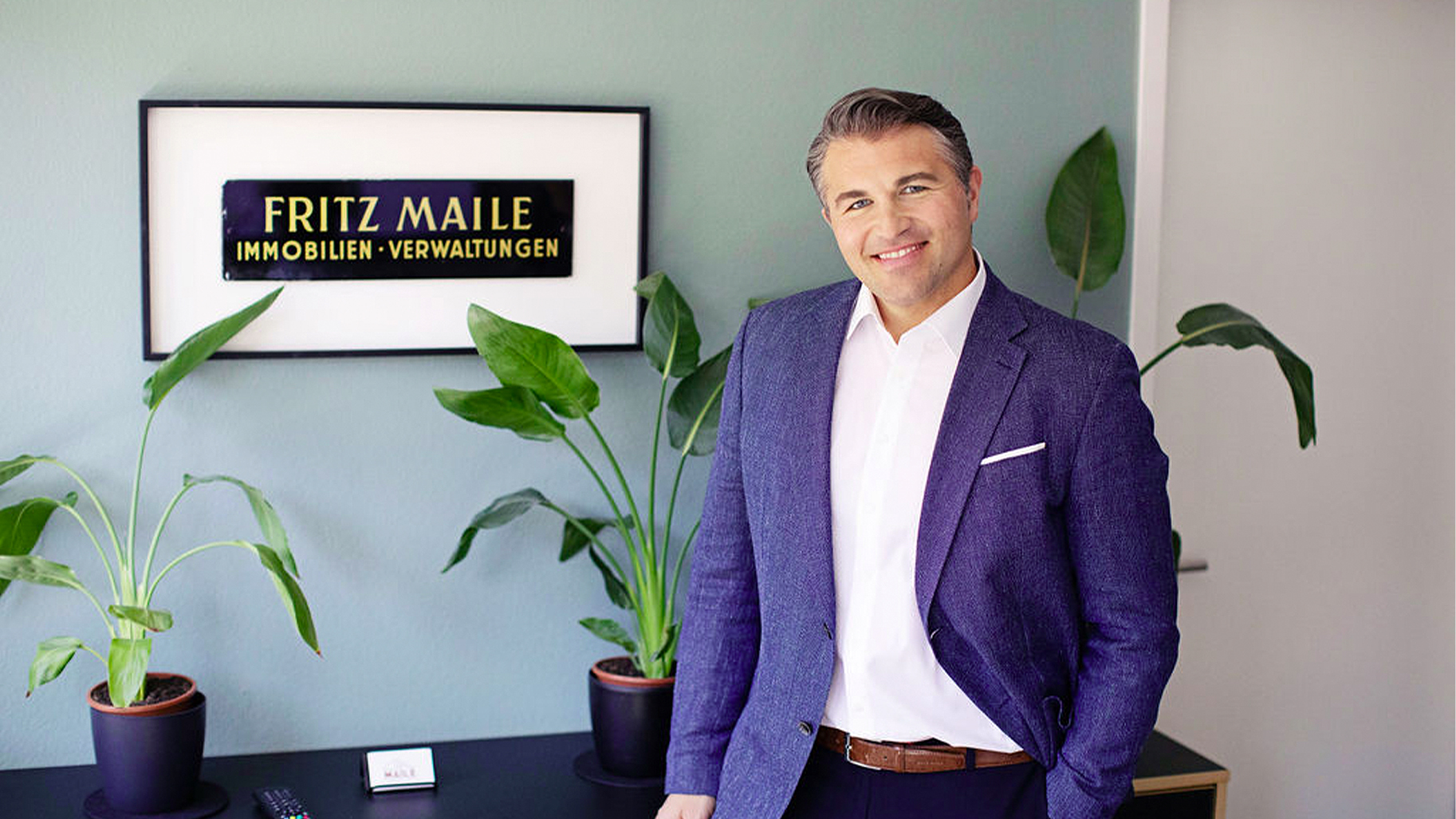 Immobilienexperte im Büro von Maile Immobilien vor dem Unternehmensschild.