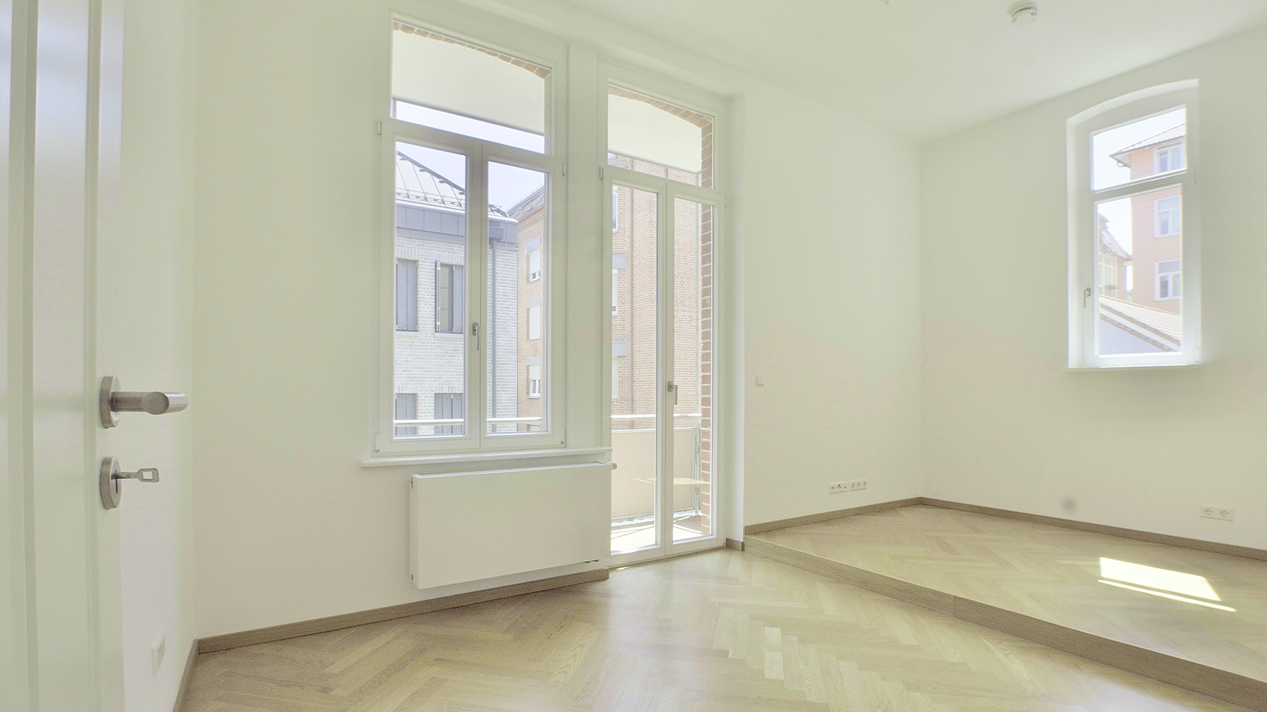 Heller sanierter Wohnraum mit Fischgrätparkett, großen Fenstern und Zugang zum Balkon