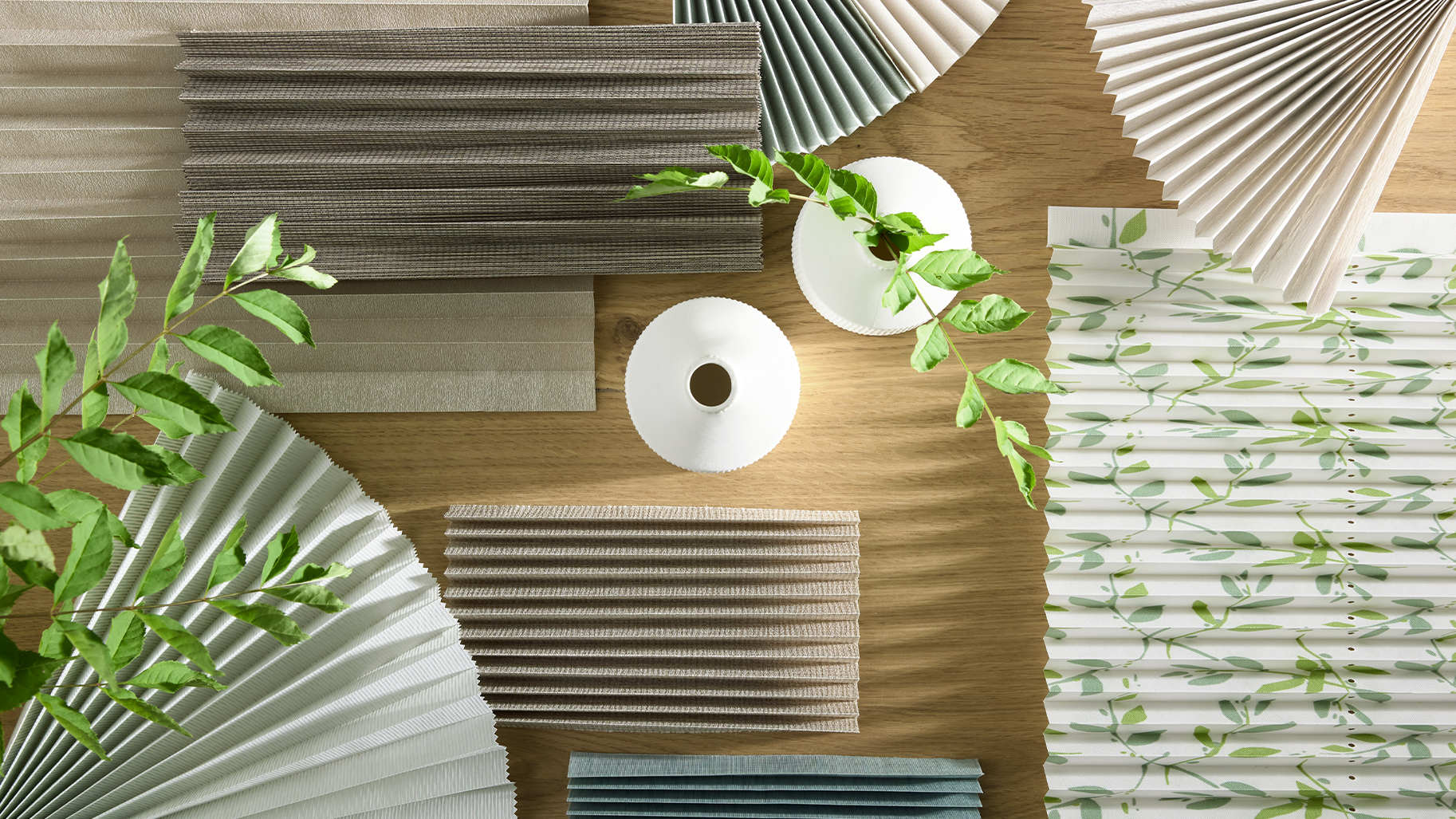 Verschiedene Plissee-Stoffmuster in Naturtönen und mit Blattdesign für individuell gestaltete Fensterbekleidung