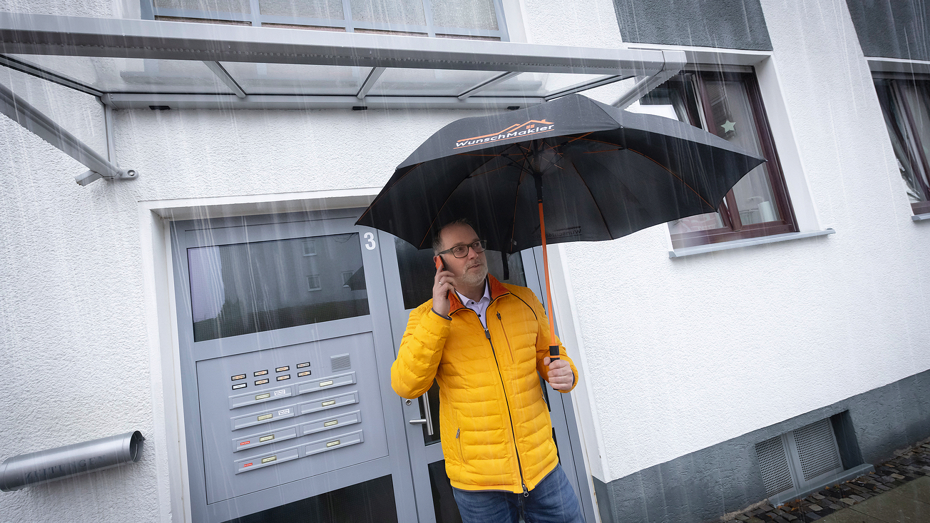 Stefan Schulte, Experte f&uuml;r Premium-Immobilien, steht im Regen vor einer Immobilie und spricht am Telefon.