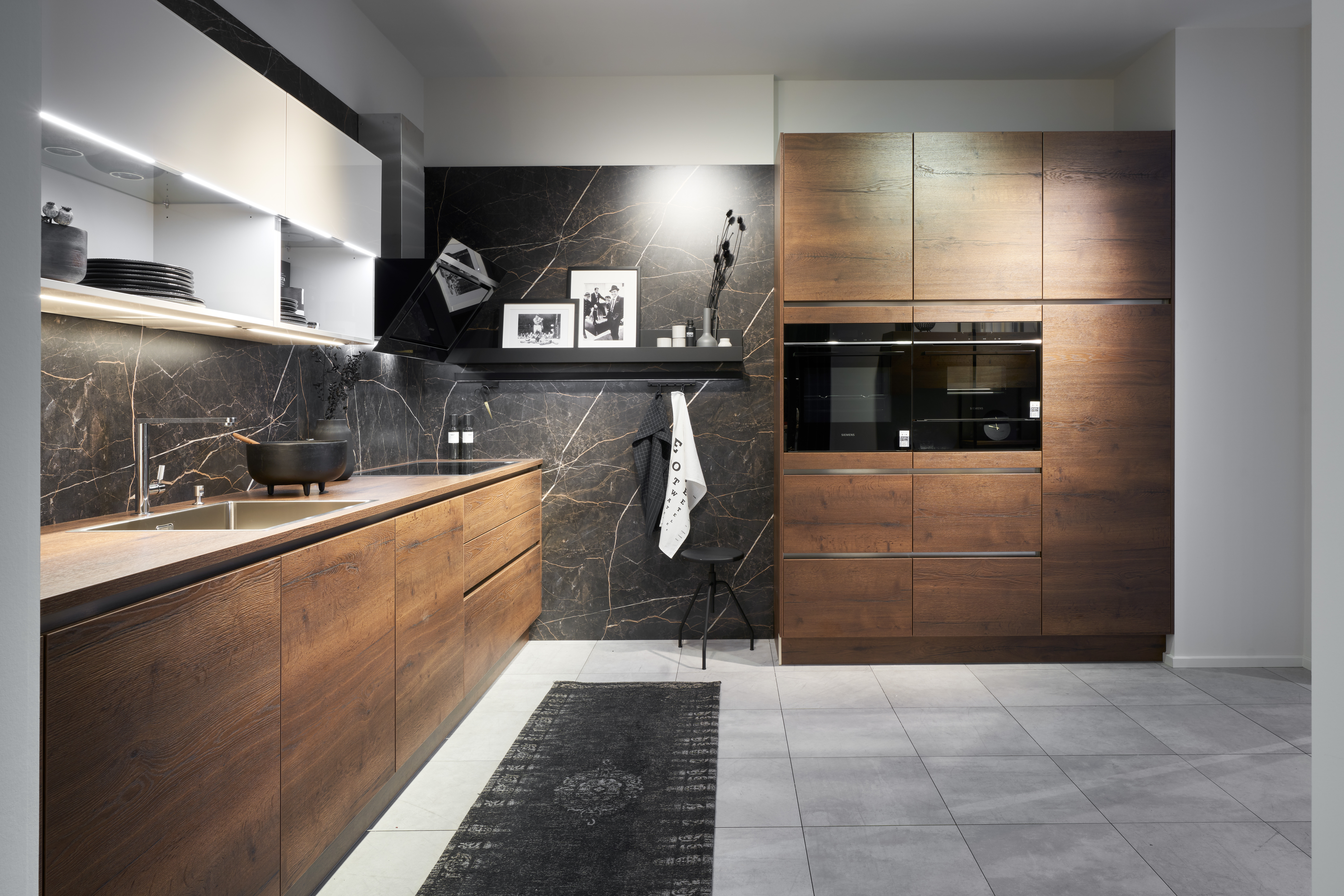 Luxuriöse Holzküche von di Vinci Kitchen in Jestetten mit dunkler Marmorwand und grifflosen Fronten in Holzoptik.