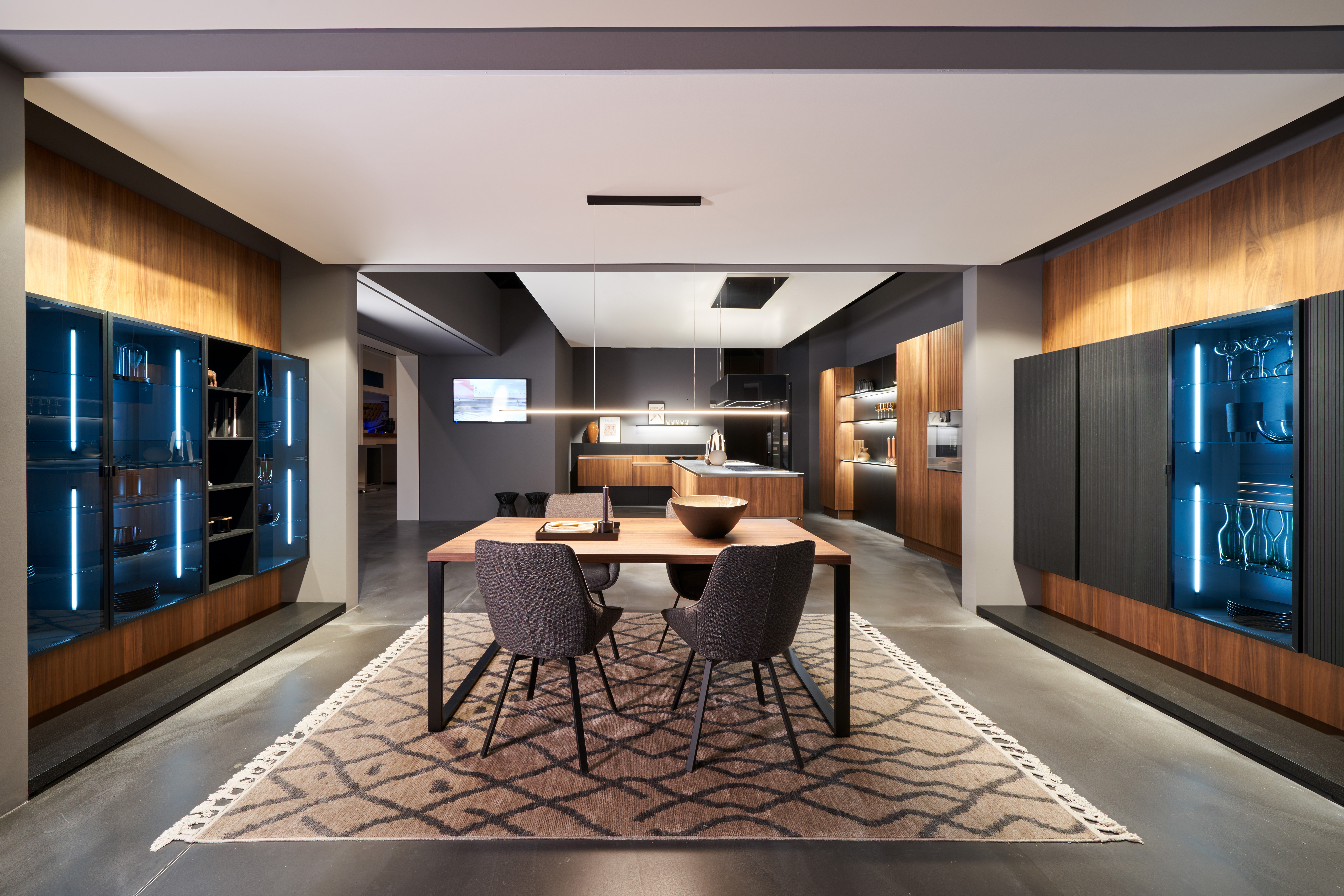 Premium-Küchenausstellung von di Vinci Kitchen in Jestetten mit Holztisch, blauer Vitrinenbeleuchtung und Küchenzeilen.