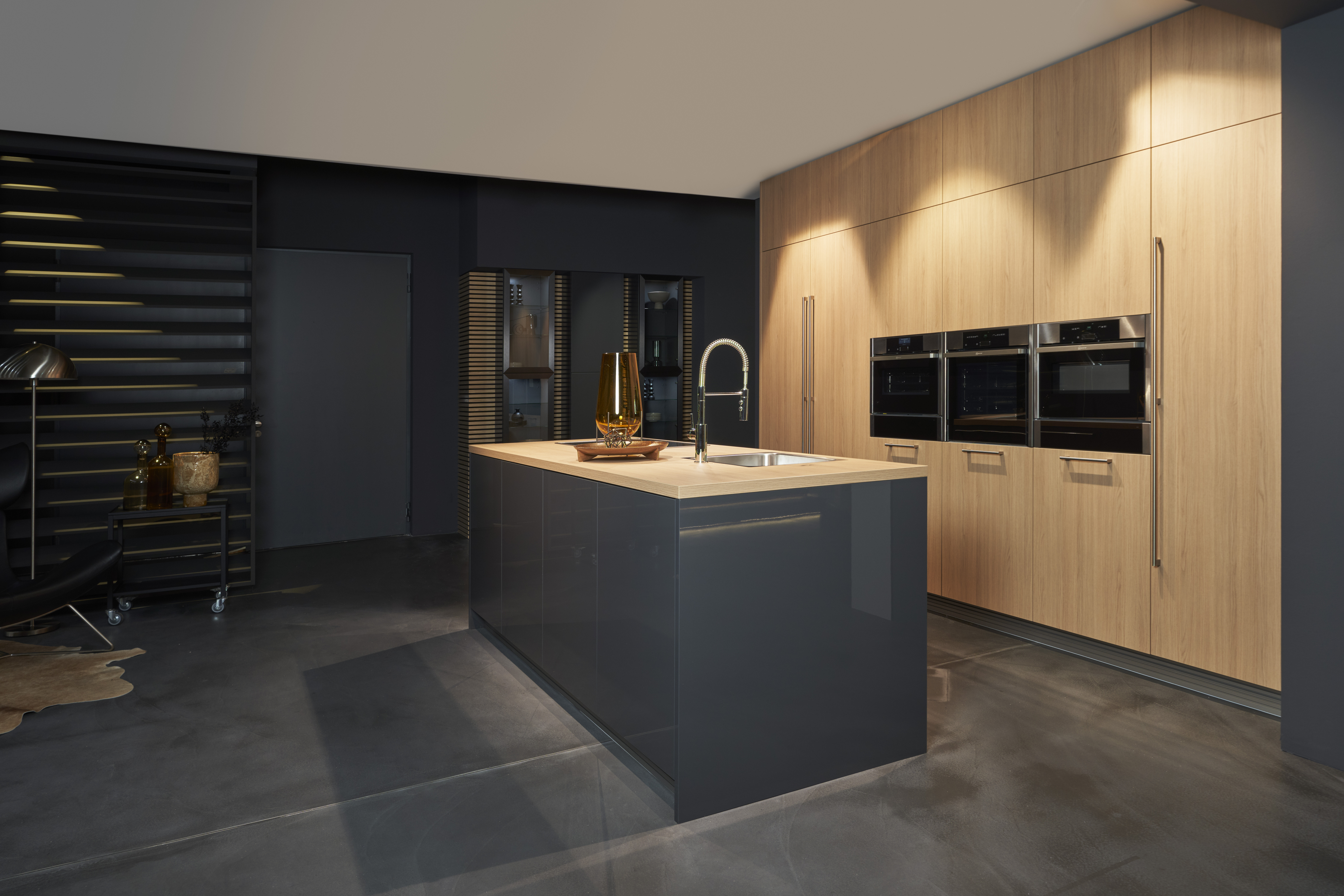 Luxusküche von di Vinci Kitchen in Jestetten mit grauer Kochinsel und integrierter Schrankwand in heller Holzoptik.