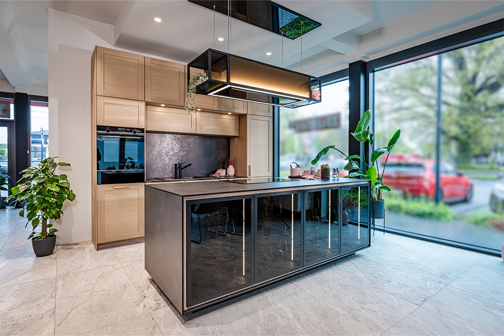 Moderne Designküche mit hellen Holzfronten, schwarzer Kochinsel, Glasvitrinen und großflächiger Beleuchtung.
