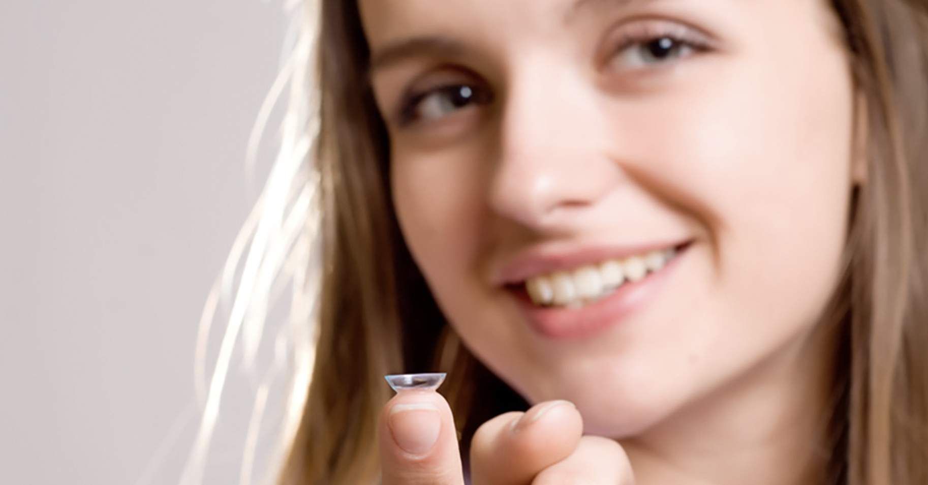 Fachkundige Anpassung von Kontaktlinsen &ndash; l&auml;chelnde Kundin pr&auml;sentiert eine weiche Kontaktlinse f&uuml;r optimales Sehen