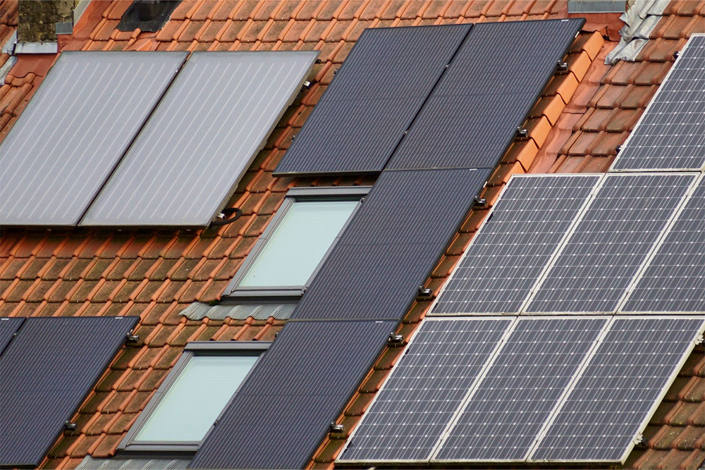 Photovoltaikmodule und Solarthermie-Kollektoren auf einem mit roten Dachziegeln gedeckten Wohnhaus.