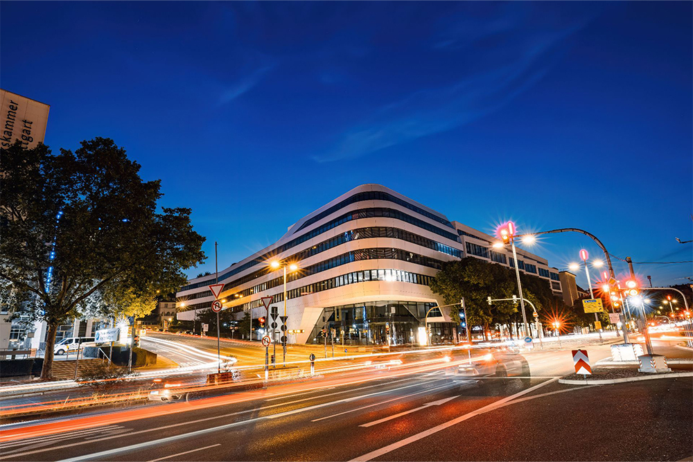 Modernes mehrgeschossiges Geschäftsgebäude an einer belebten Straßenkreuzung bei Nacht.