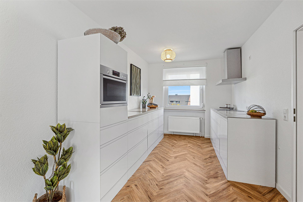 Moderne wei&szlig;e K&uuml;che mit grifflosen Schubladen und minimalistischer Einrichtung &ndash; professionelles Home Staging zur hochwertigen Pr&auml;sentation einer Immobilie beim Hausverkauf.